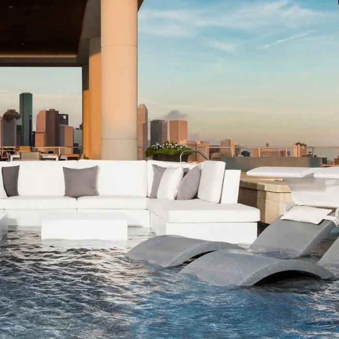 A white in-pool sectional with two grey chaise loungers in a pool with a view of the city.
