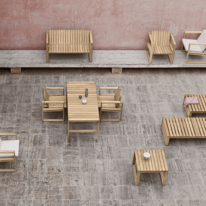A collection of teak outdoor furniture in a stone courtyard surrounded by blush pink walls.
