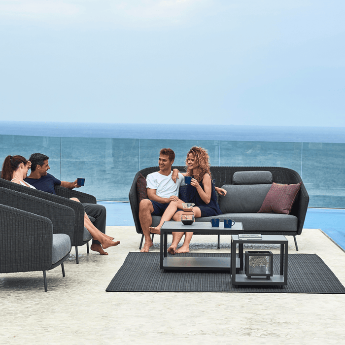 Friends talk on a sea-side patio furnished with modern outdoor furniture.