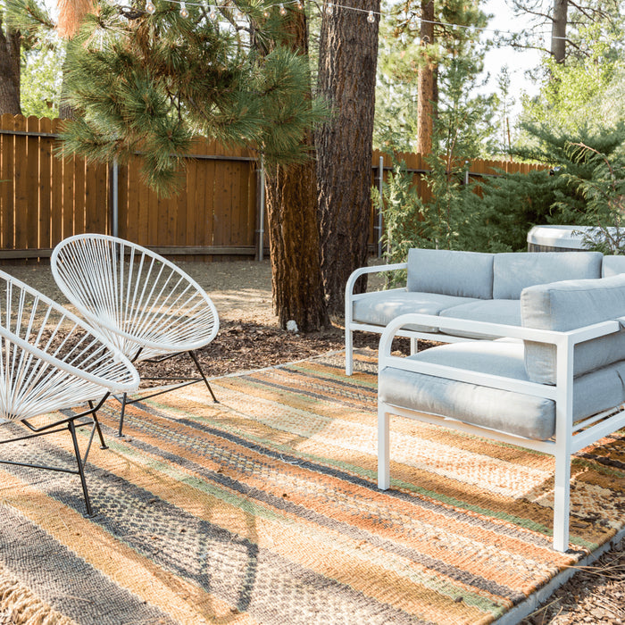 A wooded patio area featuring white Luna outdoor chairs, an outdoor a rug, and sectional.