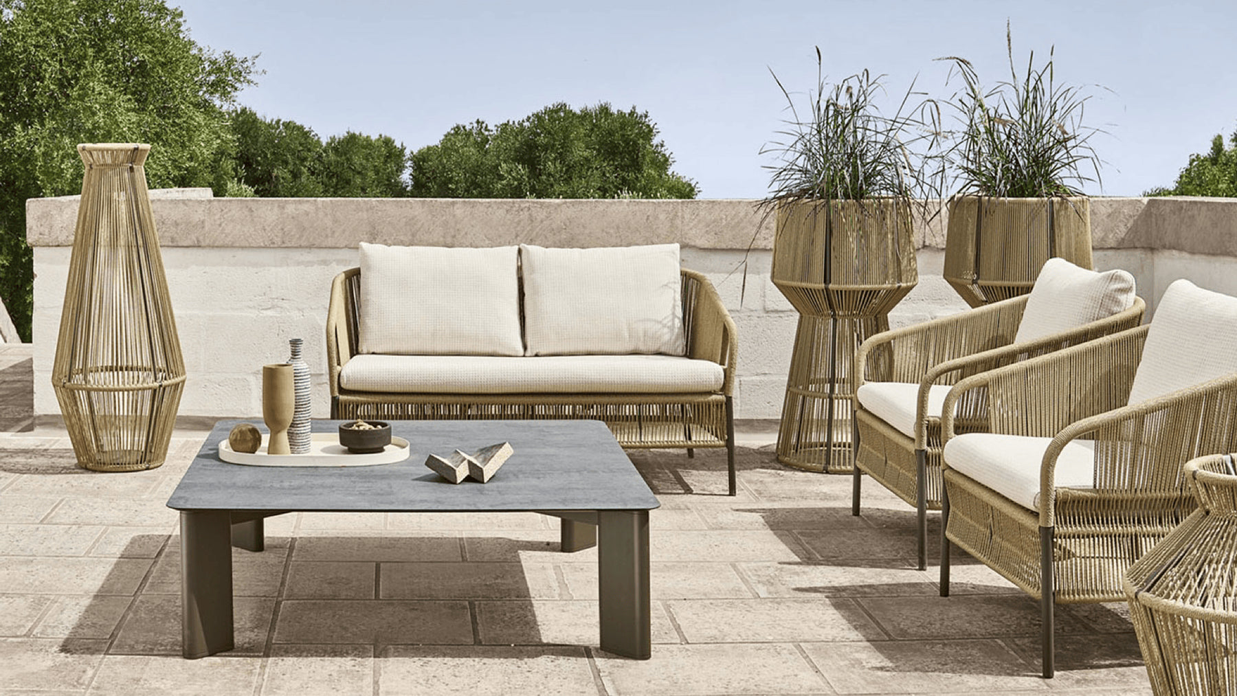 Intricate wicker outdoor lounge furniture and planters on a patio in the sun.