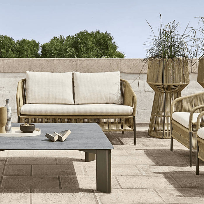 Intricate wicker outdoor lounge furniture and planters on a patio in the sun.