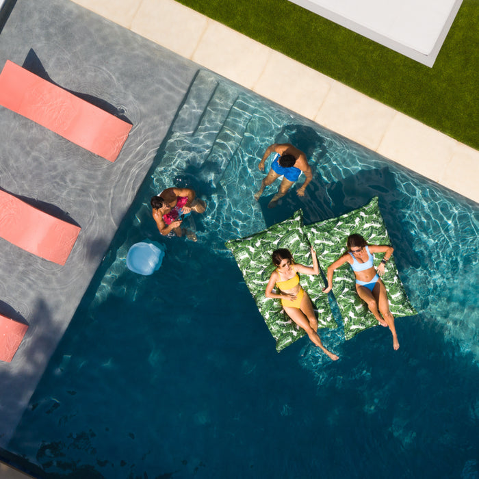 Three pink in-pool loungers on a tanning ledge while people float on in-pool pillows.
