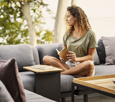 Boxhill's Mega Outdoor Side Table lifestyle image with a woman sitting down on a sofa holding a small book