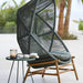 oxhill's Hive Outdoor Hanging Chair Dusty Green Frame lifestyle image with round side table at the side with candle inside the glass and a book on top