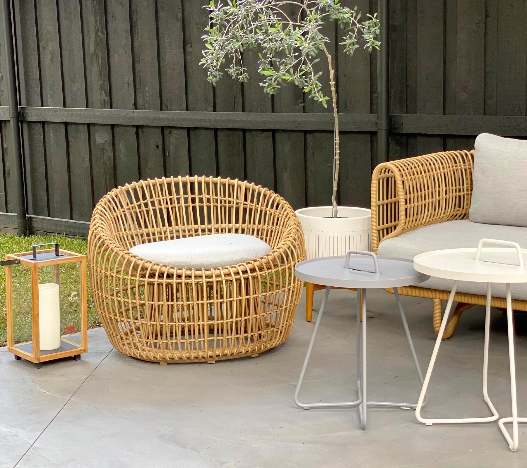 Boxhill's Nest Round Rattan Chair lifestyle image at patio with Nest 2-Seater Sofa, Lighthouse Outdoor Large Teak Lantern and 2 small round table