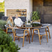 Boxhill's Luna Outdoor Dining Armchair Lifestyle image with teak round table with glass top and 2 people sitting down at patio