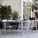 Boxhill's Ocean Outdoor Dining Armchair lifestyle image at patio with dining table and a man standing at the side holding the chair