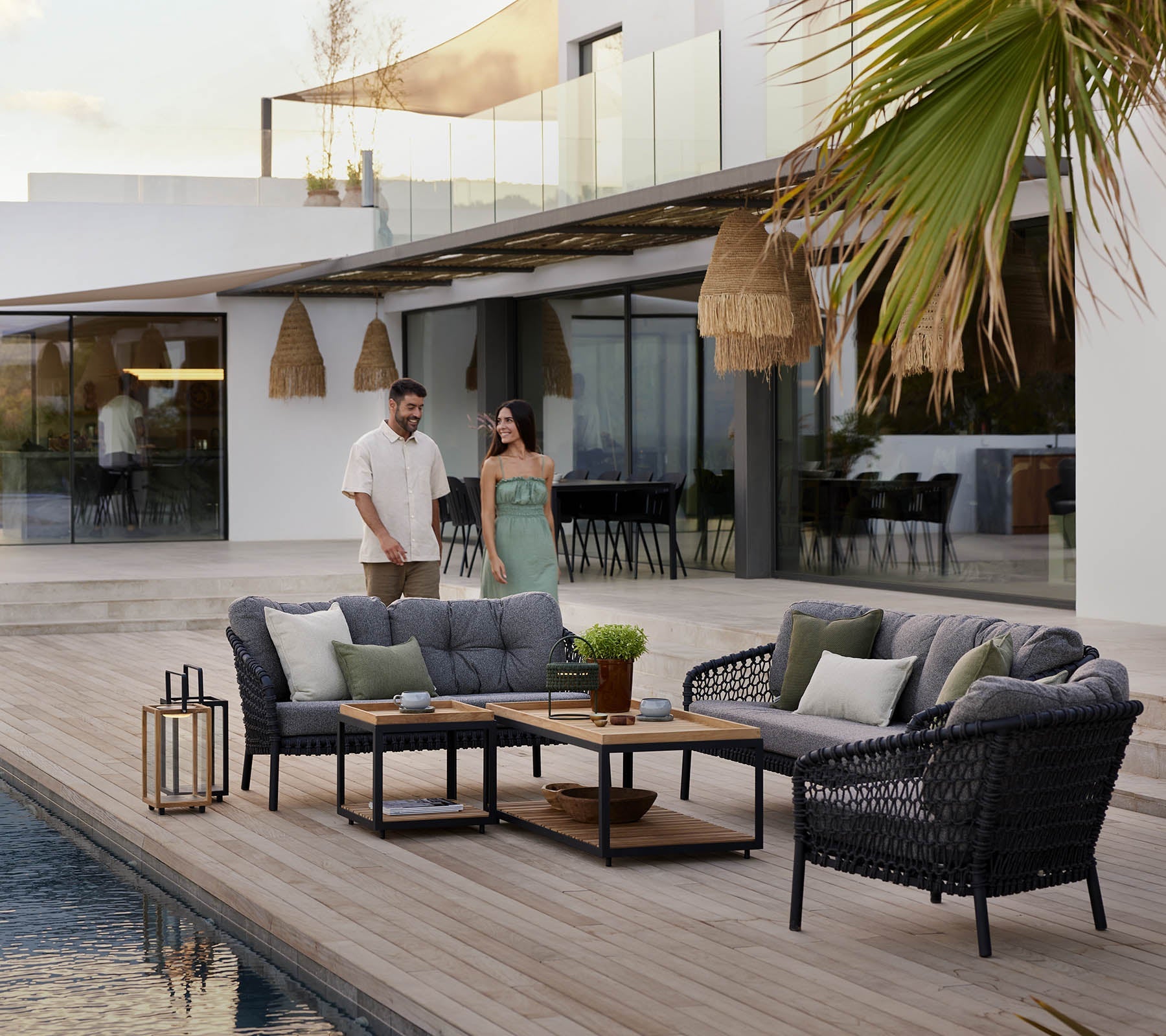 Boxhill's Ocean Large Outdoor Lounge Chair lifestyle image beside the pool with other Ocean Sofa Collection, Level Coffee Table with Teak Top and 2 people walking