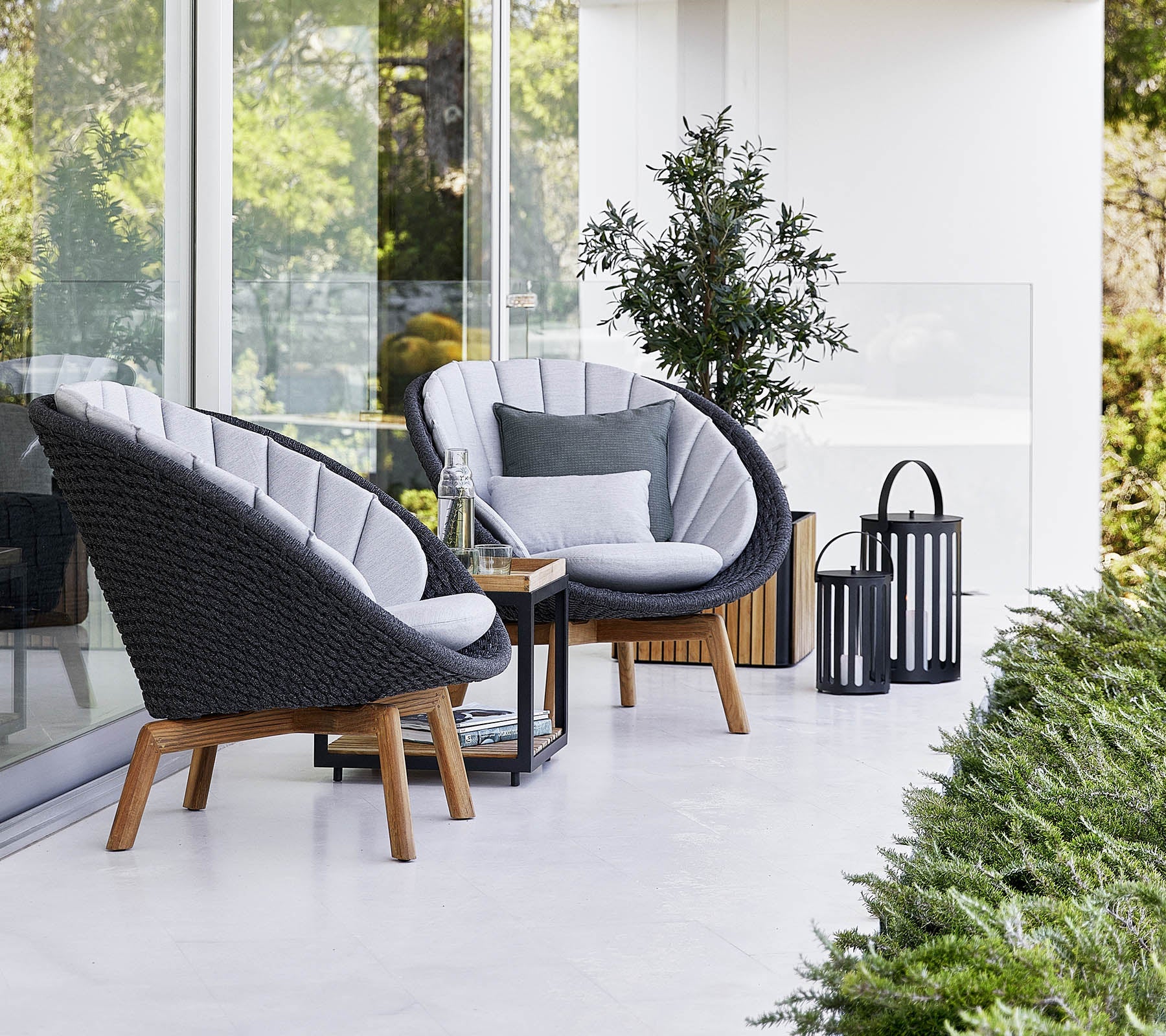 Boxhill's Peacock dark grey outdoor lounge chair with small outdoor teak coffee table placed beside glass wall