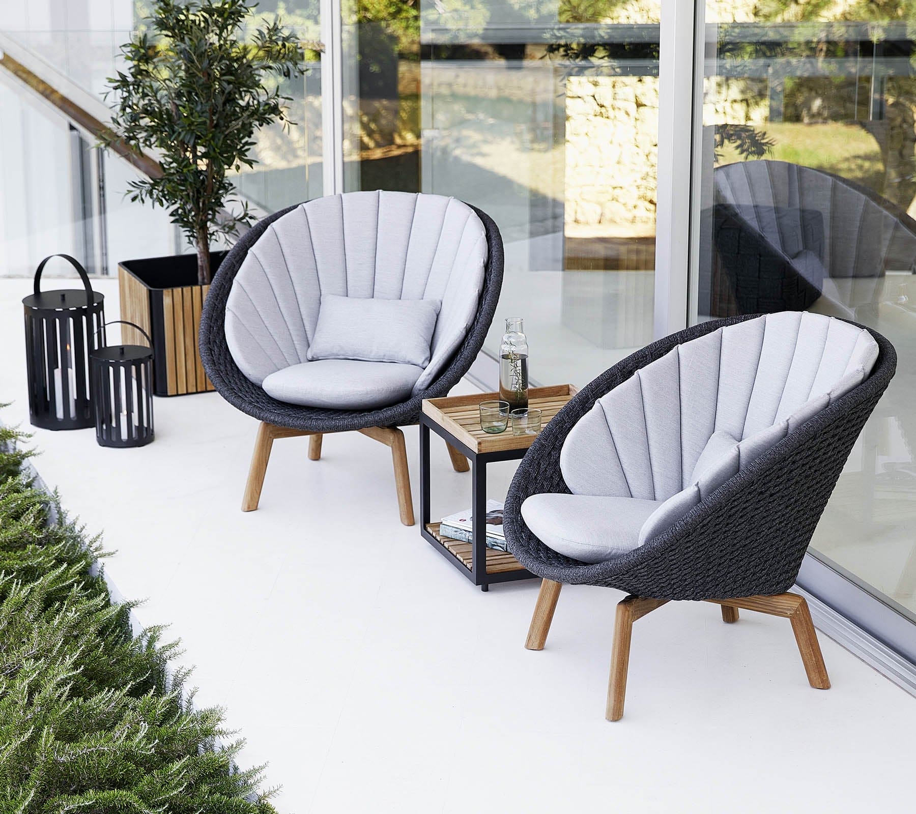Boxhill's Peacock dark grey outdoor lounge chair with small outdoor teak coffee table placed beside glass wall