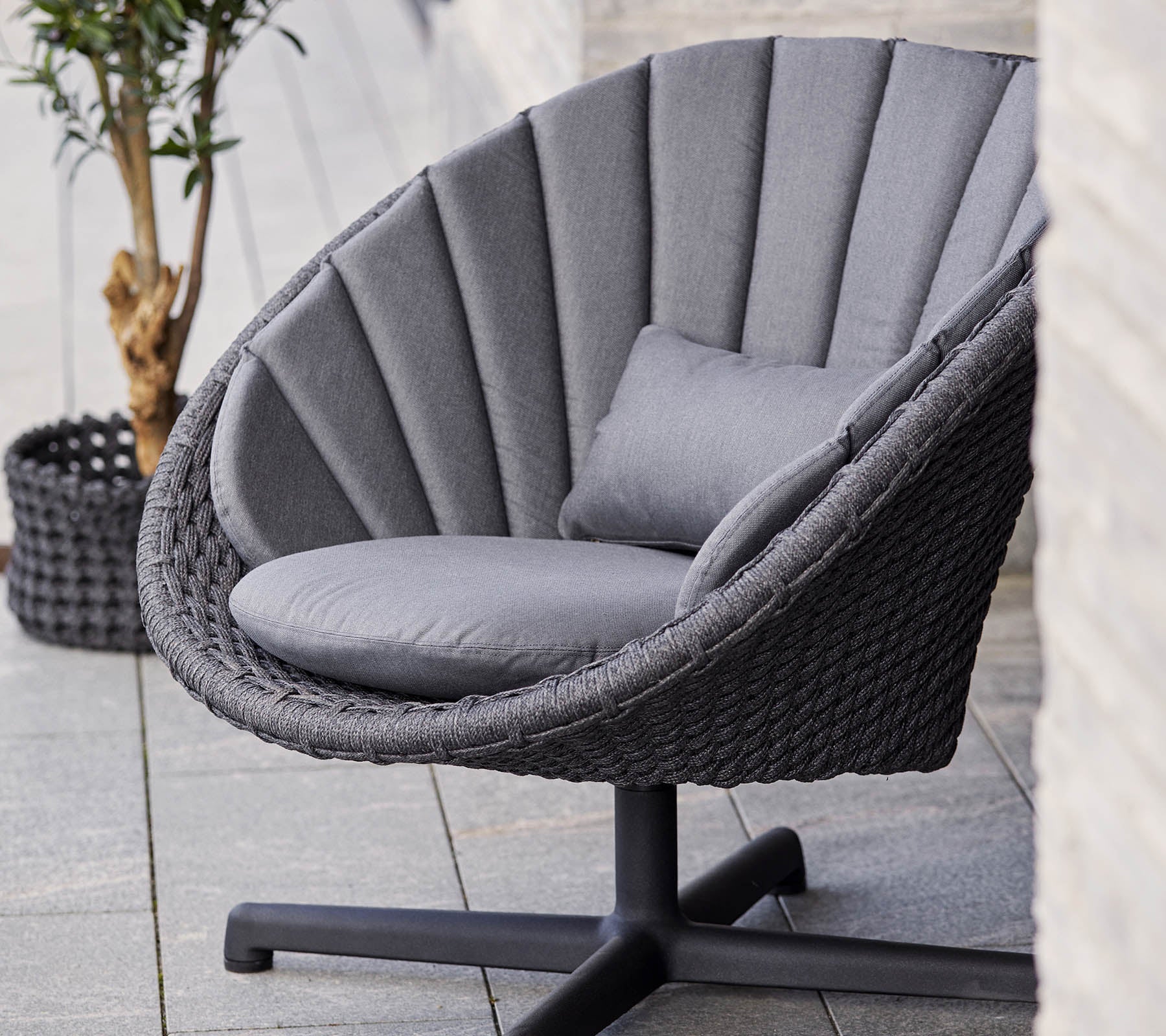 boxhill's peacock dark grey outdoor swivel lounge chair with dark grey cushion placed near to a plant in a dark grey basket