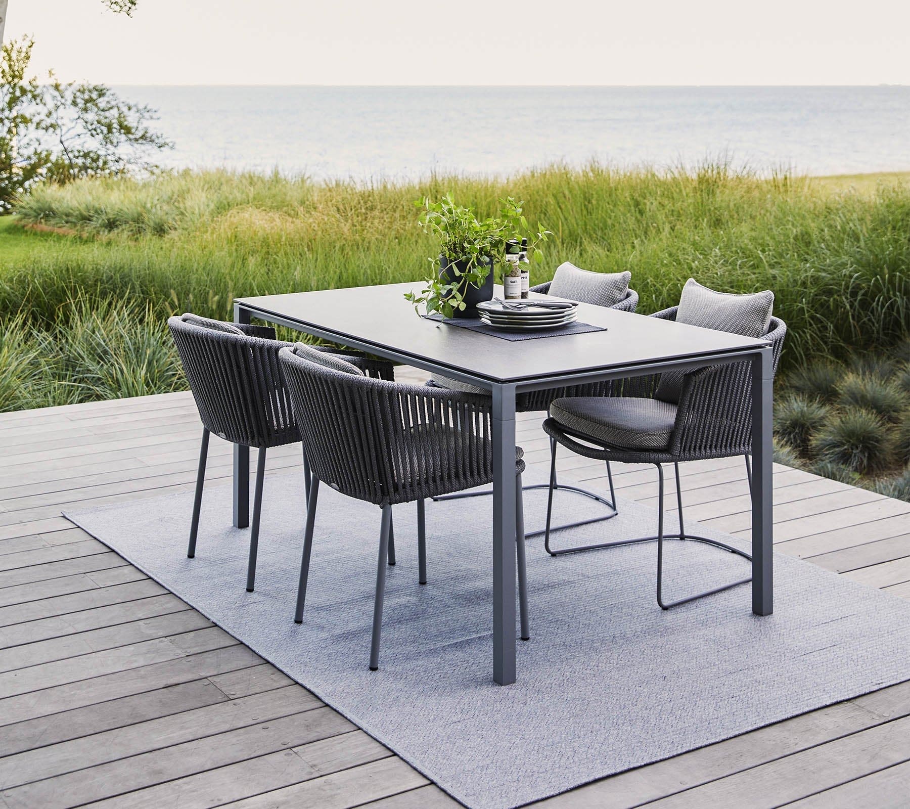 Boxhill's Pure grey aluminum outdoor dining table with grey outdoor dining chairs placed on wooden platform beside grass field