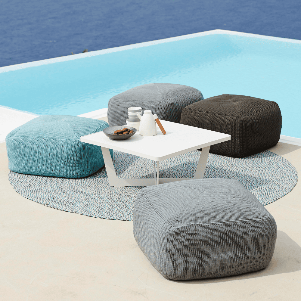 Boxhill's Divine Fabric Outdoor Footstool  lifestye image with small white square table and bowl of cookies, cup and a pot on it beside the pool