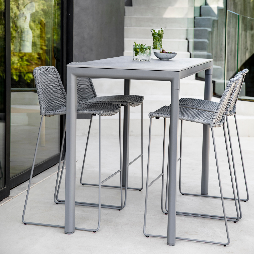 Boxhill's Drop Outdoor Bar Table Light Grey lifestyle image with Breeze Bar Stackable Chair beside glass wall near the stairs