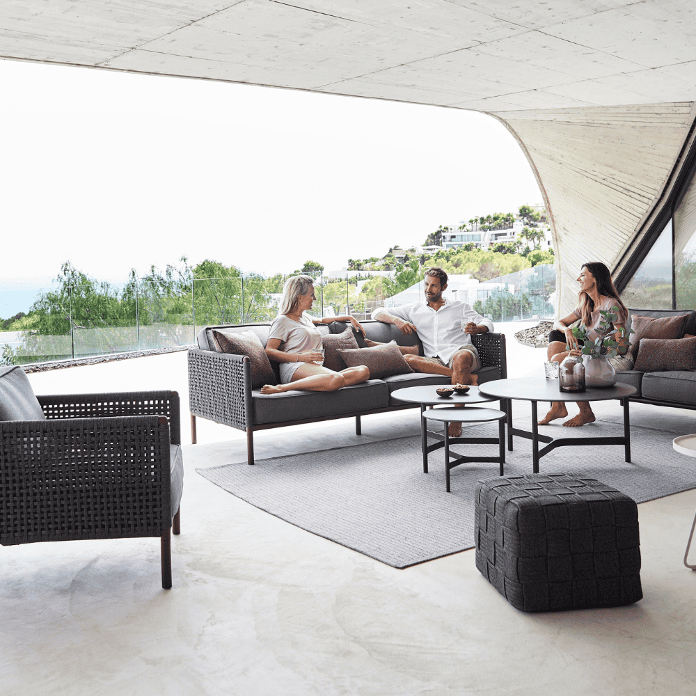Boxhill's Encore Outdoor Single Seater Grey Sofa lifestyle image at patio with Encore 2-Seater and 3-Seater Sofa, Cube Outdoor Footstool and 3 people sitting down