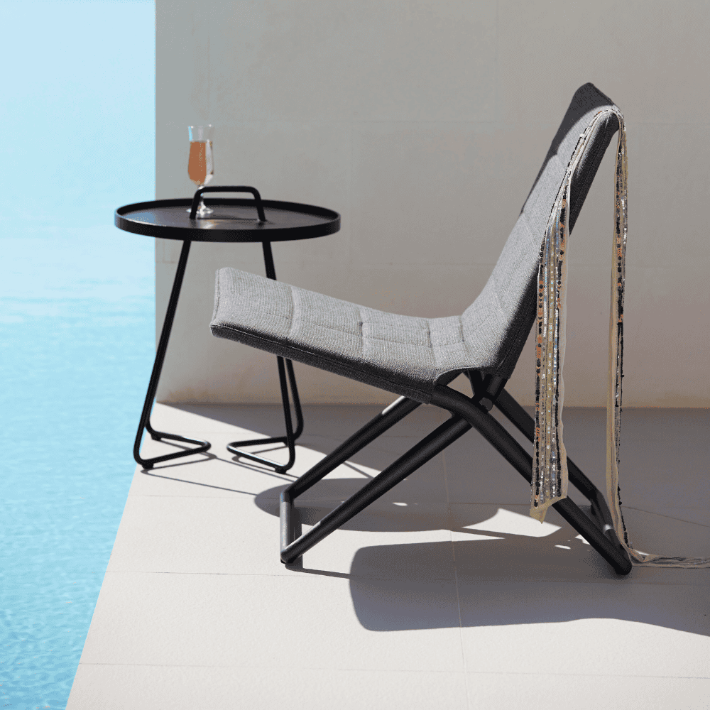Boxhill's Traveller grey outdoor folding lounge chair with dark blue outdoor round side table placed beside the pool