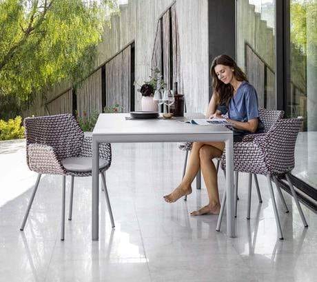 Boxhill's Vibe light grey / maroon outdoor armchair with a woman sitting on it and light grey rectangular outdoor table placed in patio 