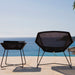 Boxhill's Breeze Outdoor Side Table Black lifestyle image with Breeze Lounge Chair at the seafront