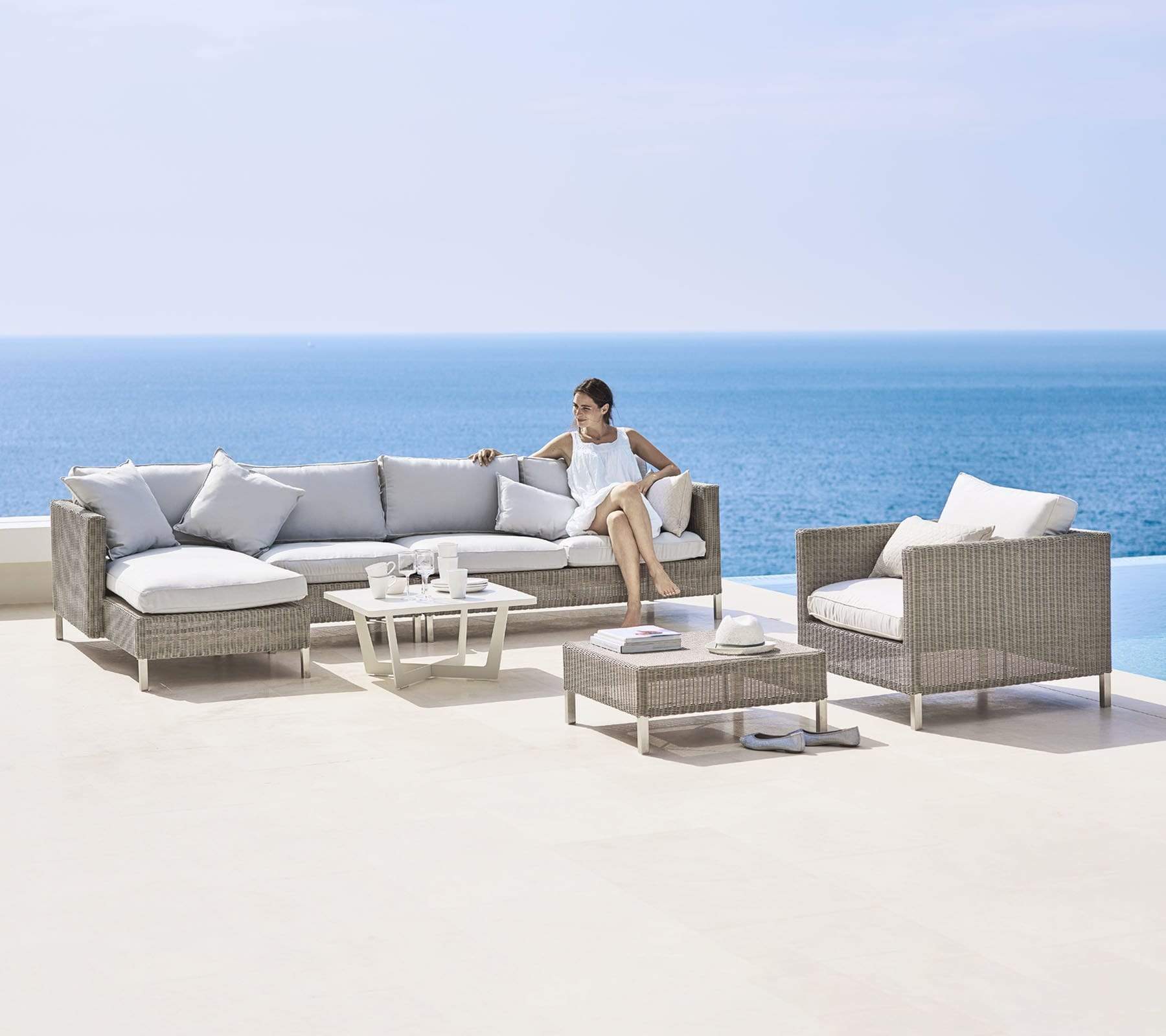 Boxhill's Connect Footstool no cushion lifestyle image beside the pool with Connect Lounge Chair and other module sofa and a woman sitting down