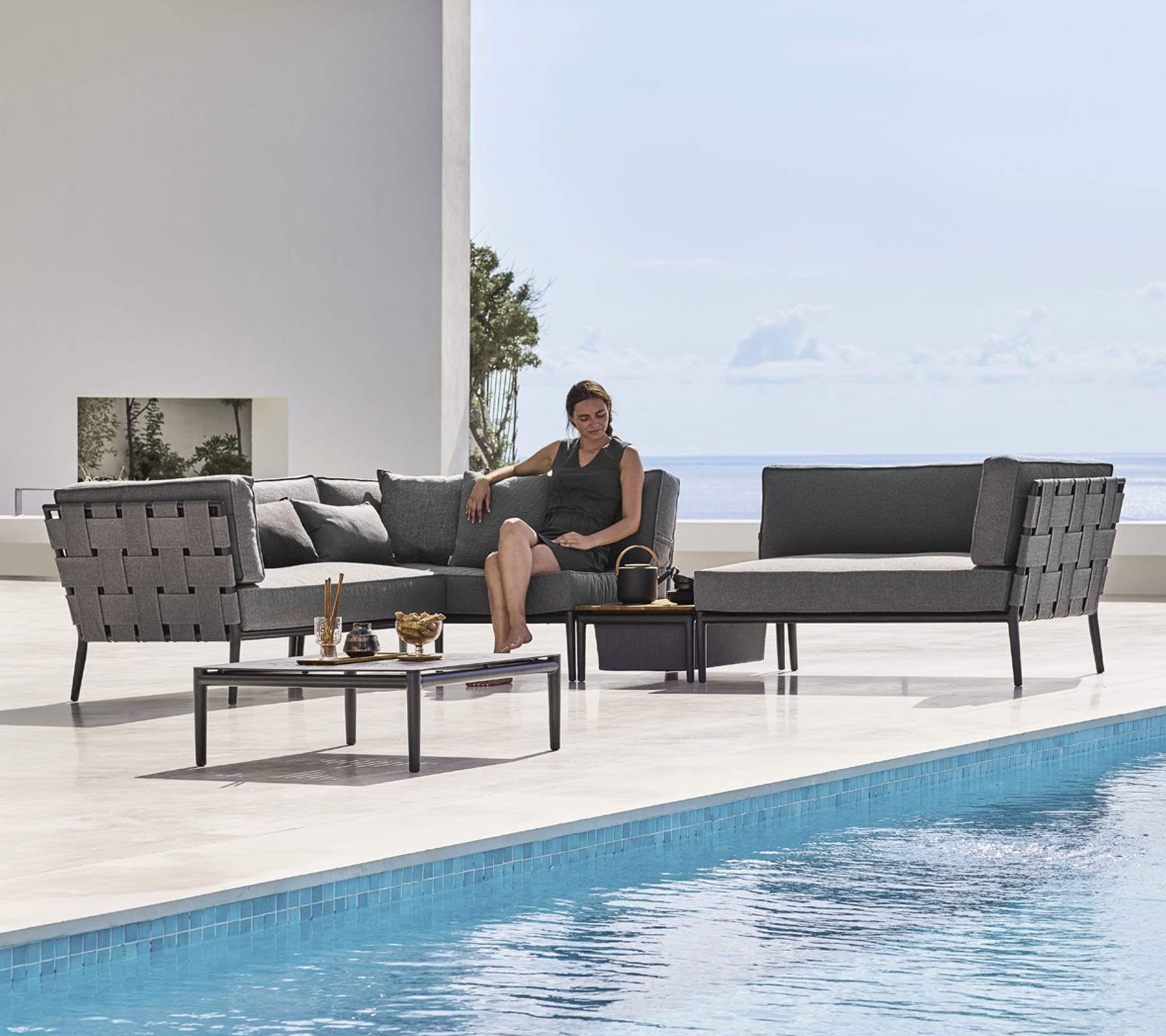 Boxhill's Conic Outdoor Coffee Table Grey lifestyle image with Conic Sectional Sofa and Conic Box Outdoor Storage Table with a woman sitting down