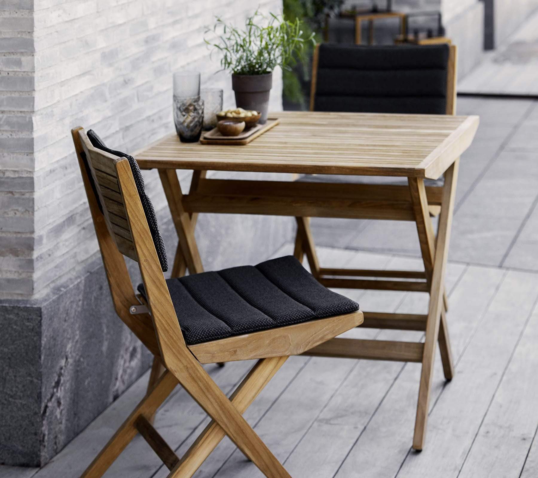 Boxhill's Flip Folding Outdoor Teak Dining chair with Dark Grey Cushion lifestyle image with Flip Folding Outdoor Teak Dining Table beside the wall at patio