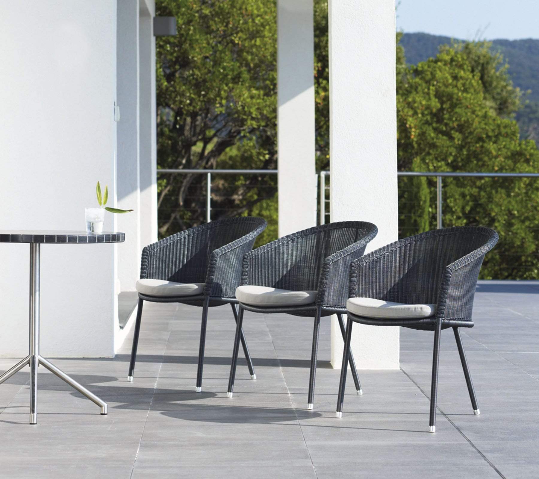  Boxhill's Trinity dark grey outdoor stackable chair w/ white cushion and stainless steel base round table placed on balcony