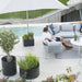 Boxhill's lava grey outdoor round medium modern planter box with man and woman sitting on light grey sectional sofa beside the pool