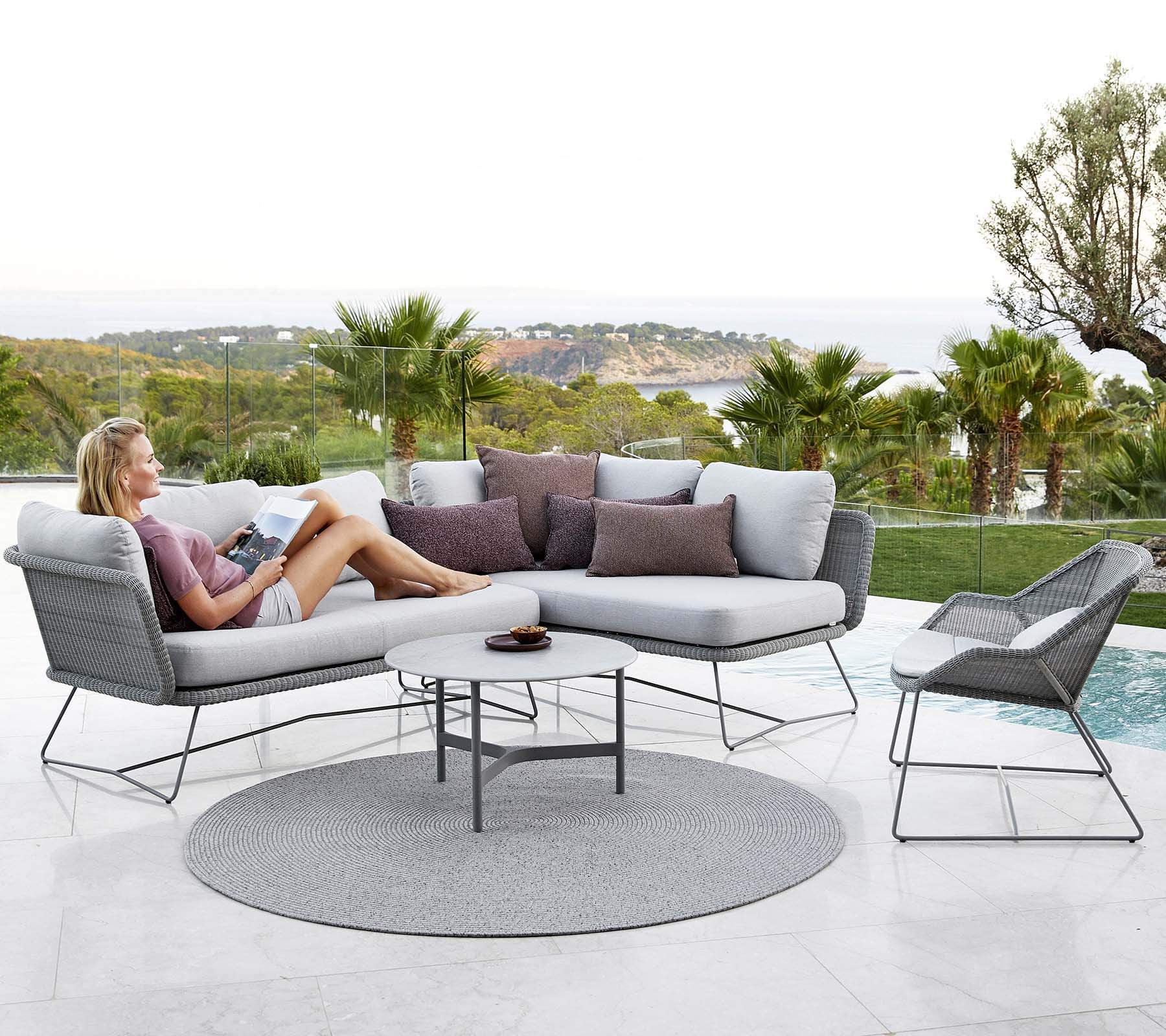 Boxhill's Circle Outdoor Rug Grey lifestyle image with 2 seater sofa and chaise lounge with a woman sitting down beside the pool