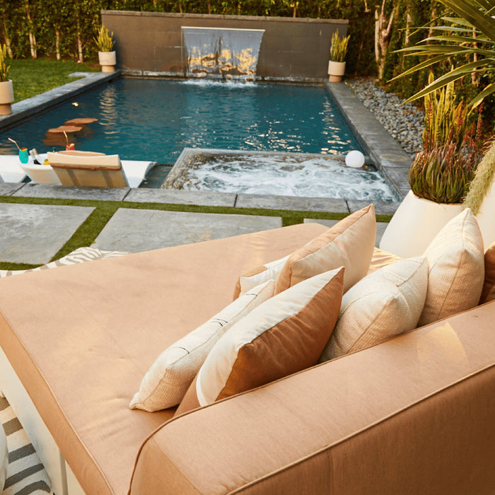 A pool deck day bed overlooks a pool with fountain and two in-pool chaise loungers.