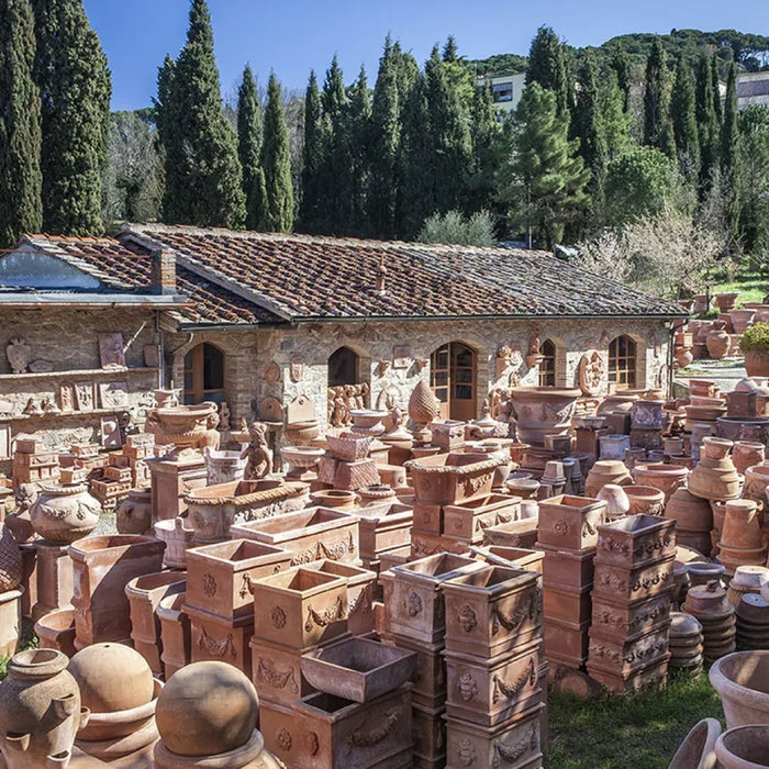 Outdoor courtyard at a terracotta workshop in Impruneta, Italy, filled with handmade Italian terracotta planters, vases, and garden sculptures surrounded by cypress trees and traditional stone buildings.