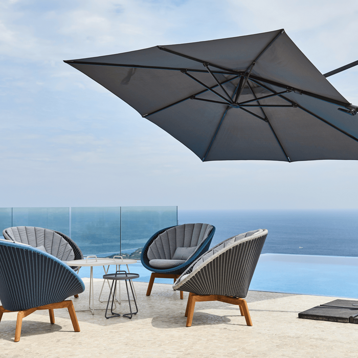 A large cantilever umbrella shades 4 high-backed chairs on a seaside patio.
