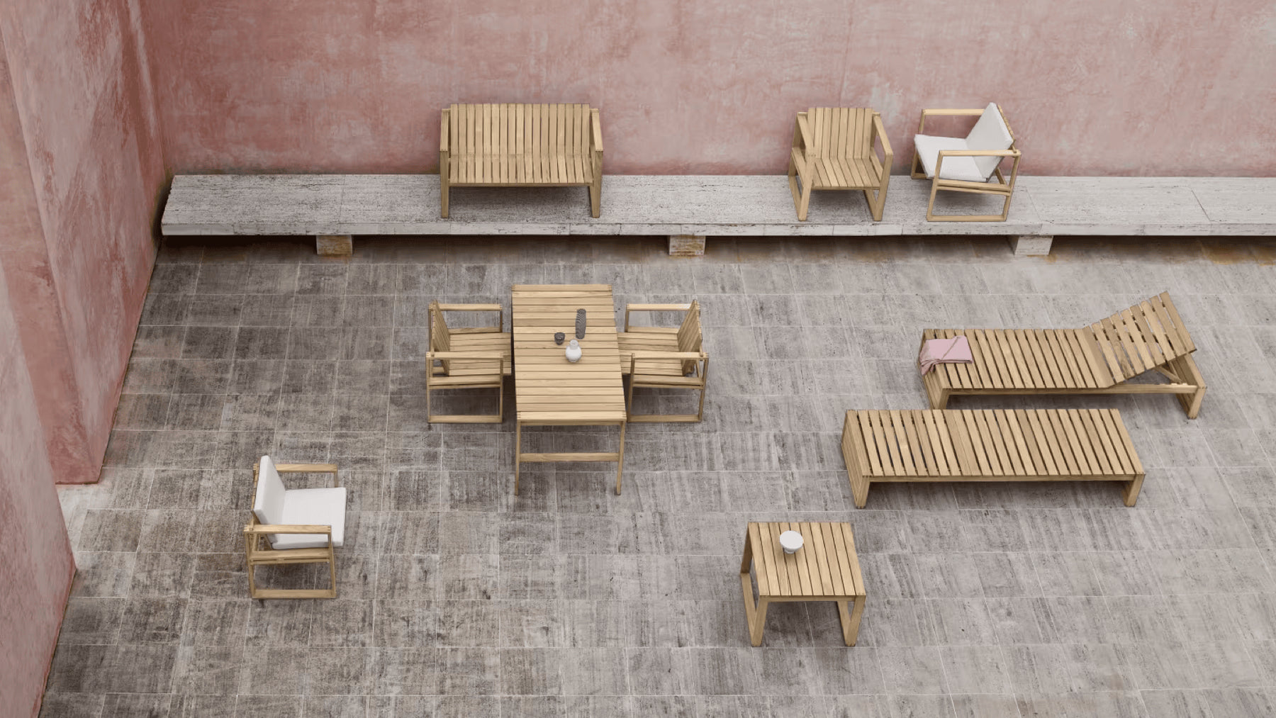 A collection of teak outdoor furniture in a stone courtyard surrounded by blush pink walls.