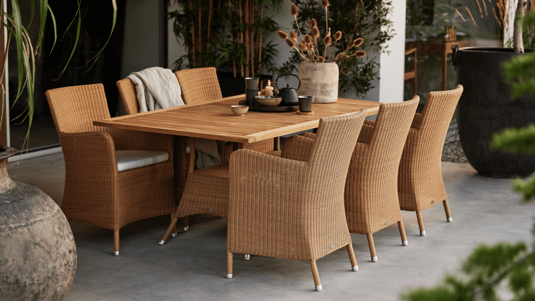 Danish loom-weave style outdoor dining chairs around teak table.