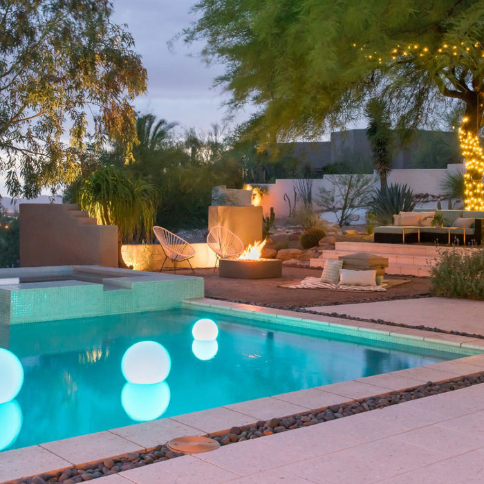 An modern outdoor pool at night with floating glow balls and a fire place glowing behind it.