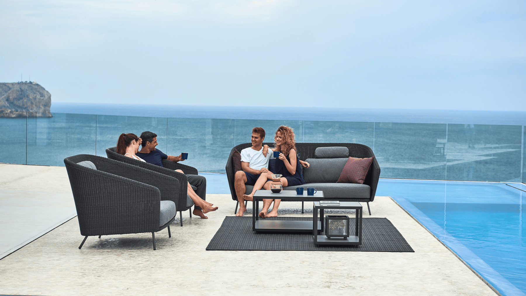 Friends talk on a sea-side patio furnished with modern outdoor furniture.