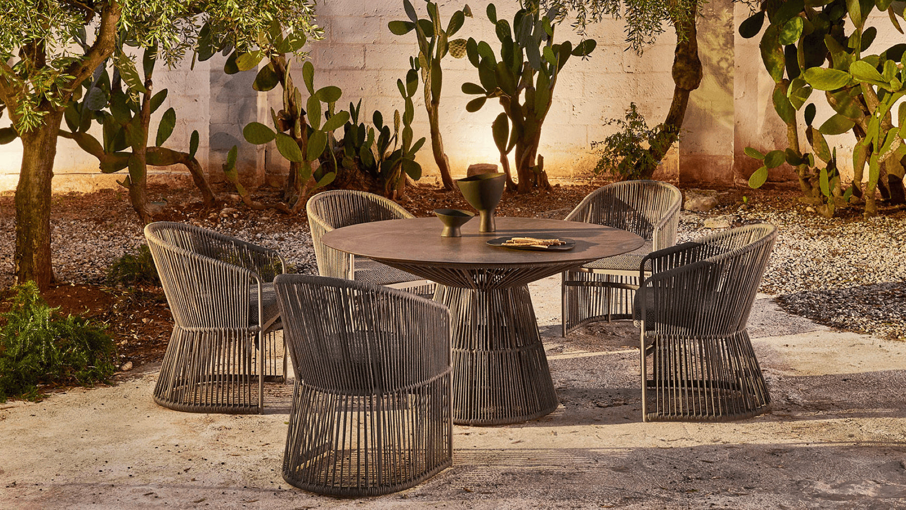 Curved woven dining armchairs in a desert garden at night.