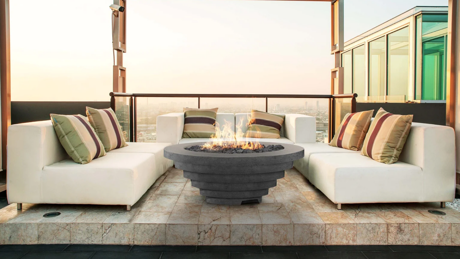 A tiered concrete fire pit flanked by white sofas is the focal point of this outdoor lounge space. 