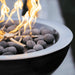Close-up view of a round outdoor copper fire bowl with lava rocks with flame rising from its stainless-steel burner