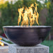A round outdoor copper fire bowl with flames on top placed on a concrete pedestal