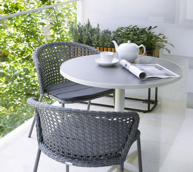 Boxhill's Drop Round Outdoor Cafe Table White lifestyle image on balcony with cup, tea pot and magazine on top, and 2 dining chairs and plants at the side