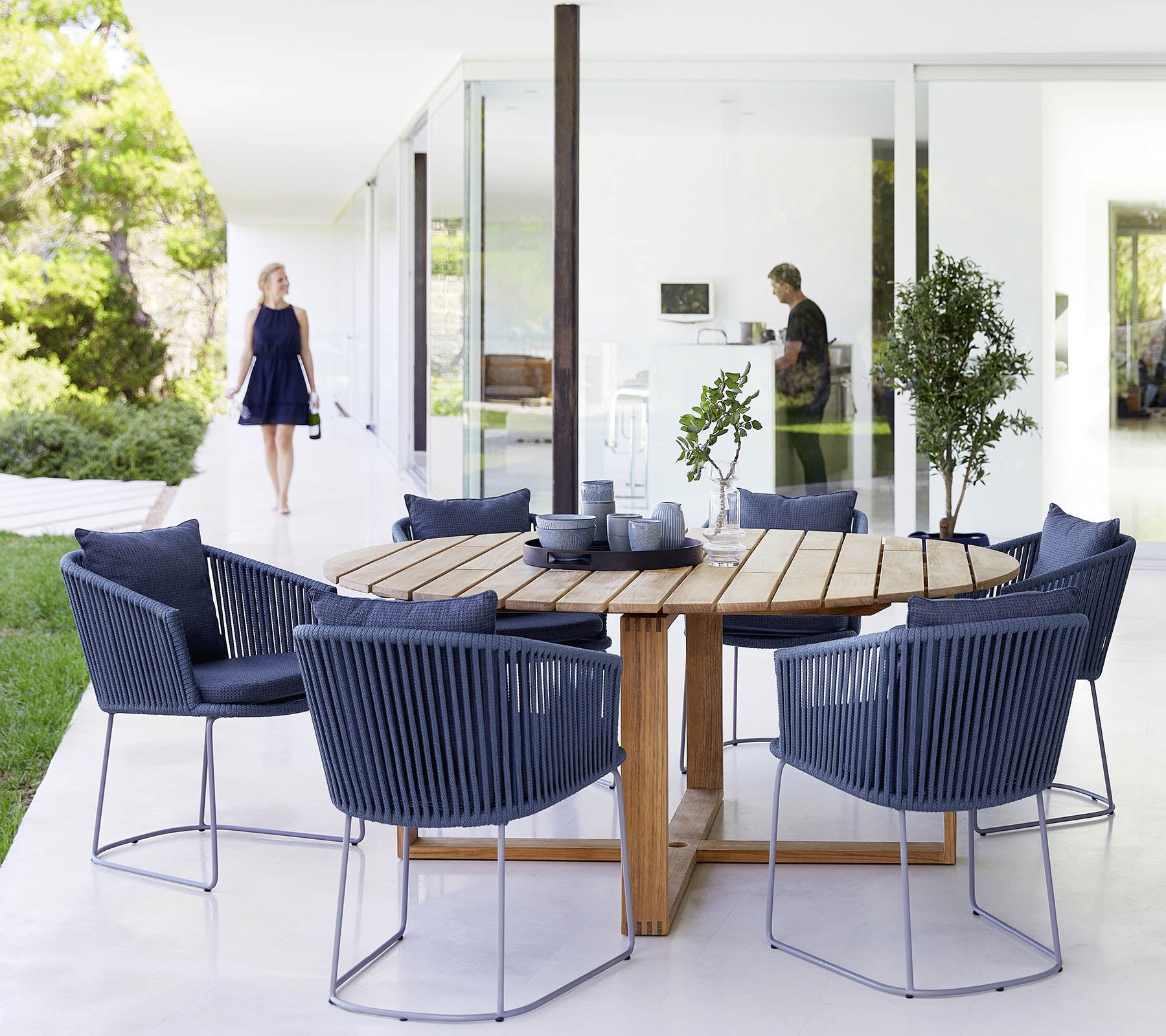 Endless Outdoor Round Dining TableBoxhill's Endless Outdoor Round Dining Table lifestyle image with cups and bowls on top, and 6 blue dining chairs at patio