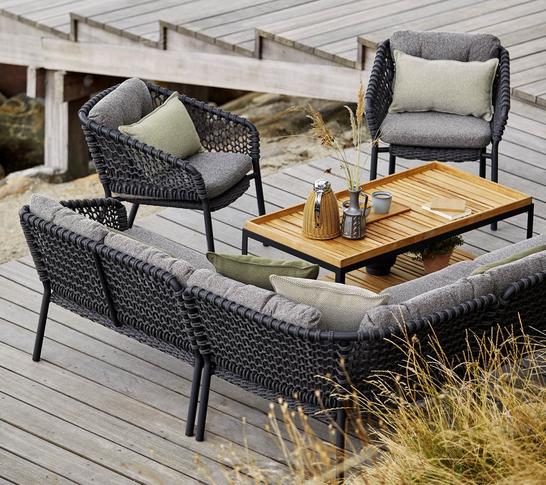Boxhill's Ocean Outdoor Corner Sofa Module lifestyle image with other Ocean Module Sofa and Chair Collection, and Level Coffee Table with Teak Top on wooden platform beside seashore