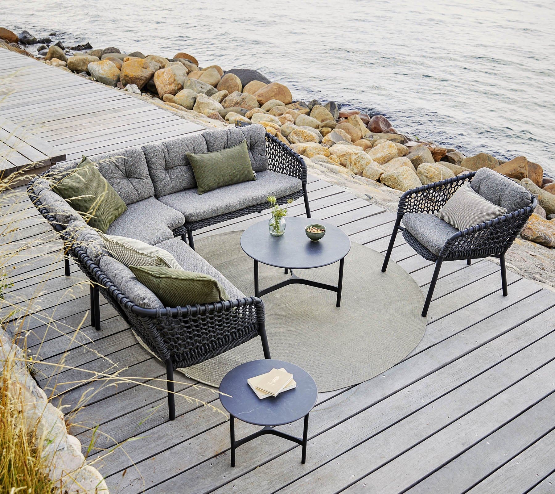 Boxhill's Ocean Outdoor Corner Sofa Module lifestyle image with other Ocean Module Sofa and Chair Collection, and 2 round table on wooden platform beside rocky seashore