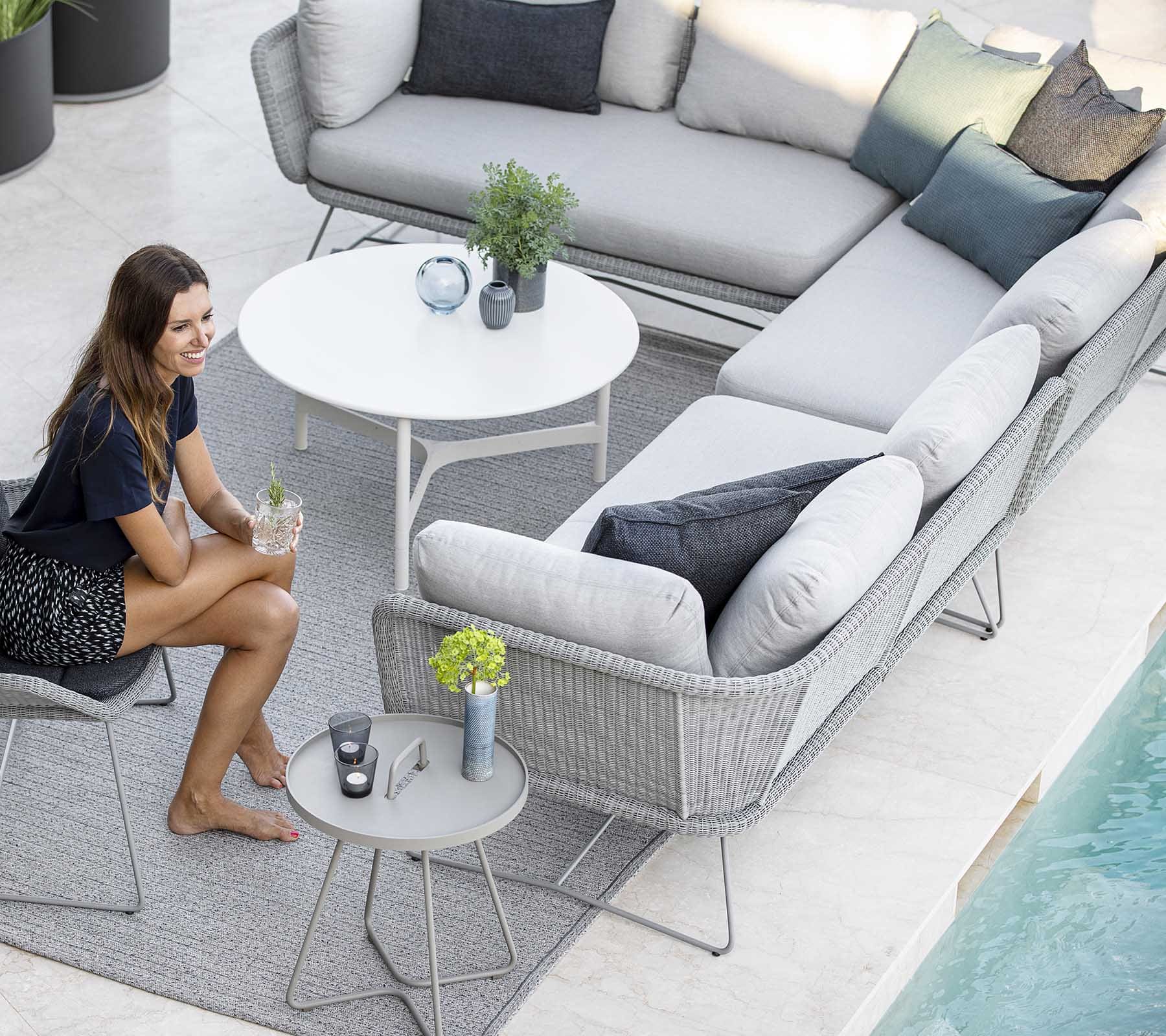 Boxhill's Horizon 2-Seater Outdoor Left Module Sofa lifestyle image together with Horizon 2-Seater Outdoor Right Module Sofa at patio with a white round table and a woman sitting down holding a glass of water