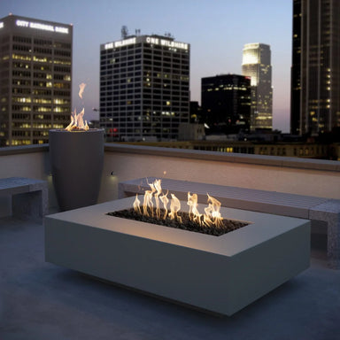 Gray outdoor concrete rectangular fire pit with flames set on a roof top patio with a view city skyline with tall buildings