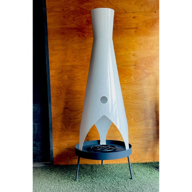 Tall, unique modern outdoor metal fire pit placed on a green lawn against a wooden wall