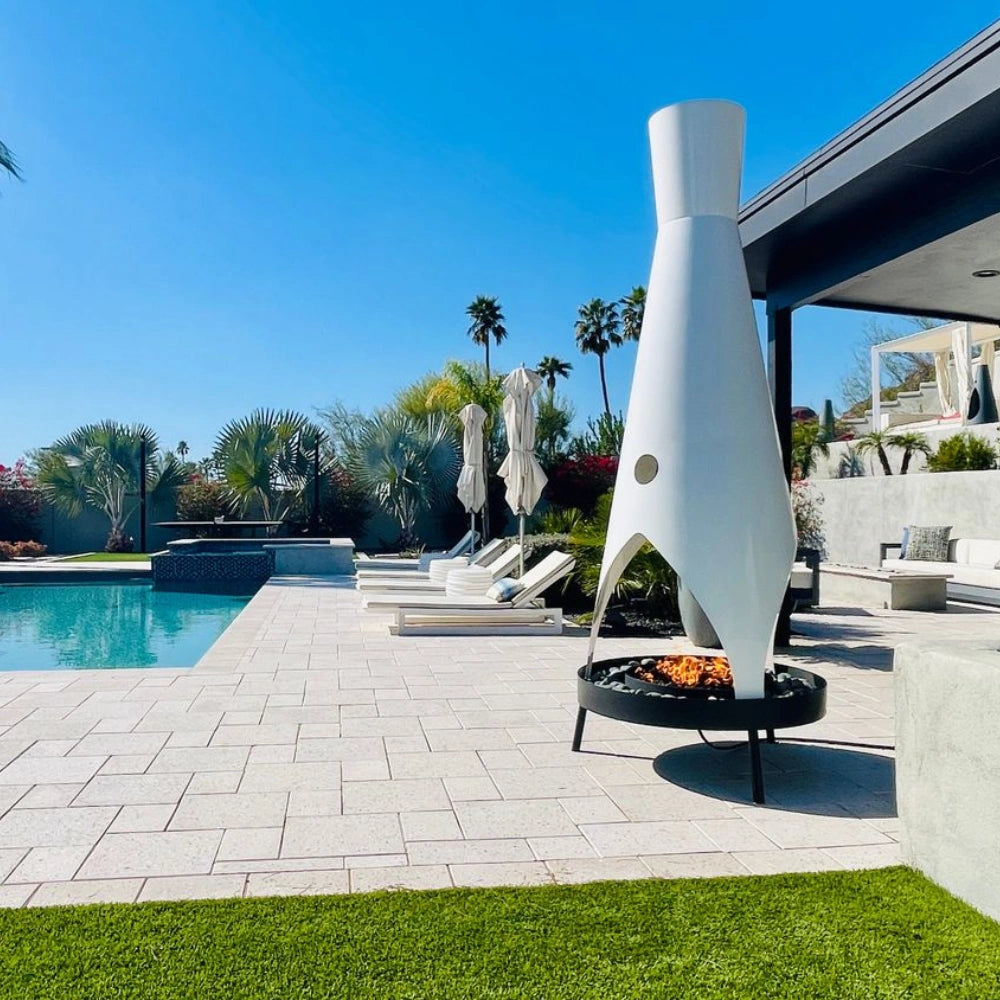 Tall white modern outdoor metal fire pit with a stylish design placed on a patio near a pool area