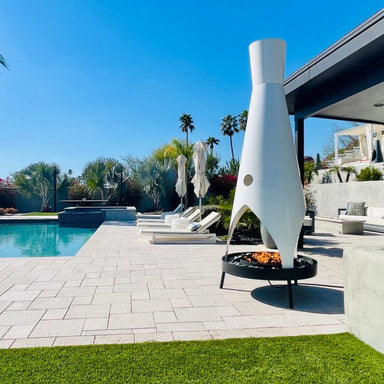 Tall white modern outdoor metal fire pit with a stylish design placed on a patio near a pool area