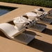 Three modern white in-pool chaise loungers with black-and-white headrests and three poolside tables with water glasses beside the pool.
